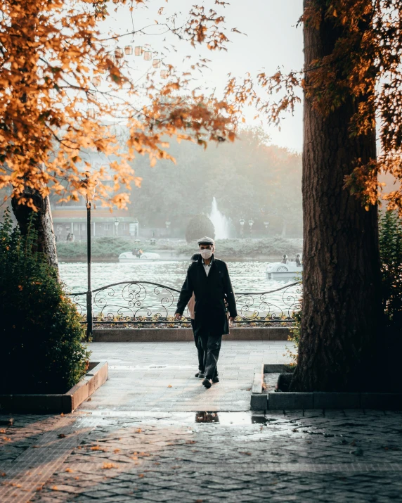 a man wearing a black hat walks on a pathway in the rain