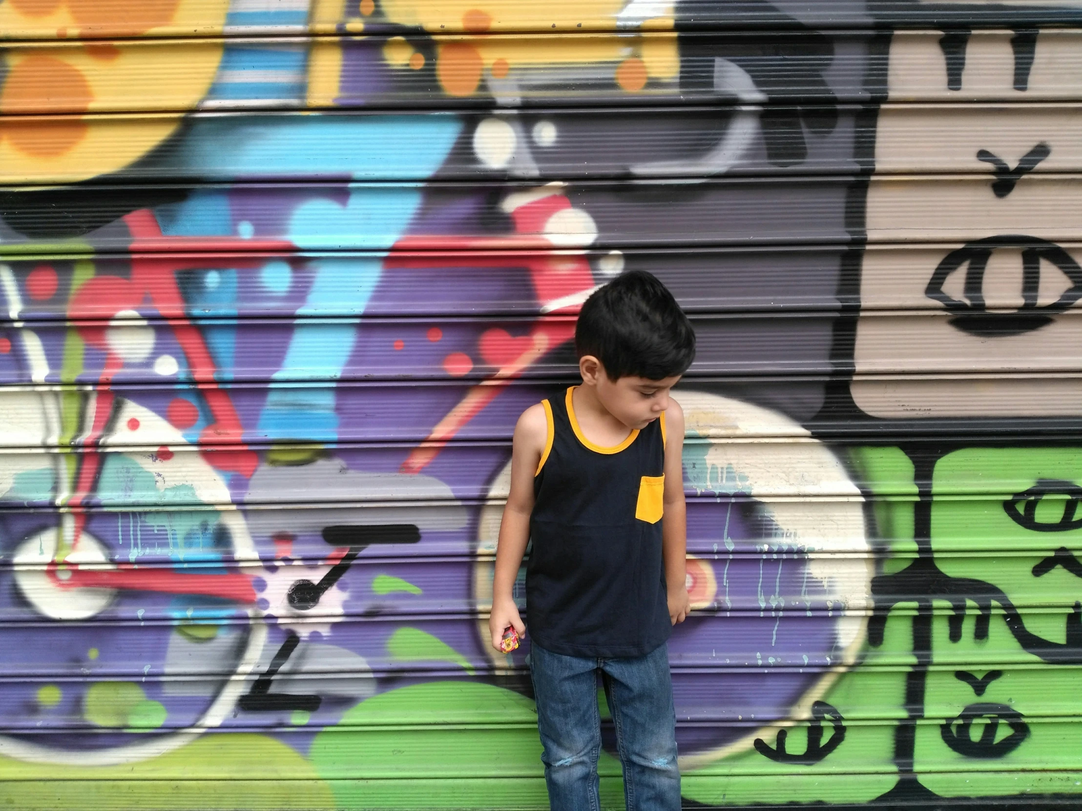 the small boy stands in front of the graffiti painted garage door