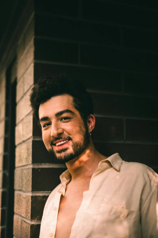 a man smiling as he stands in front of a brick wall