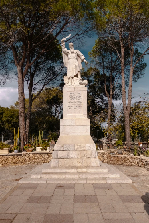 a statue on top of a white base surrounded by trees