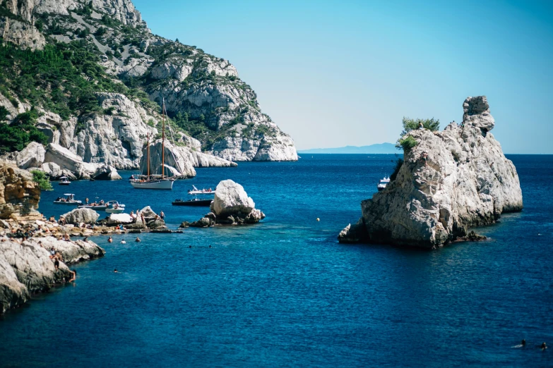 several sail boats in the water near rocky cliffs