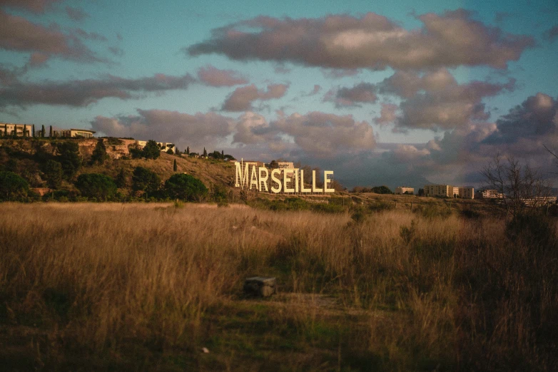 a rusted sign in a field with a large hill on the far side