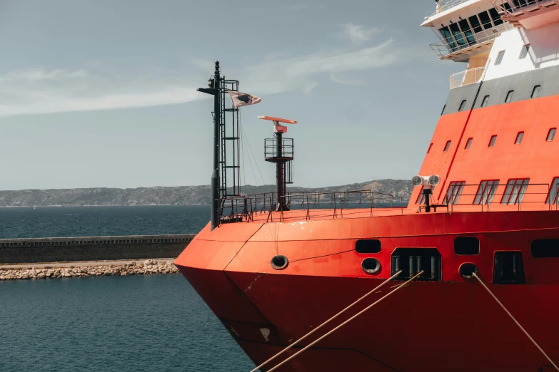 the side of a large red ship next to the shore