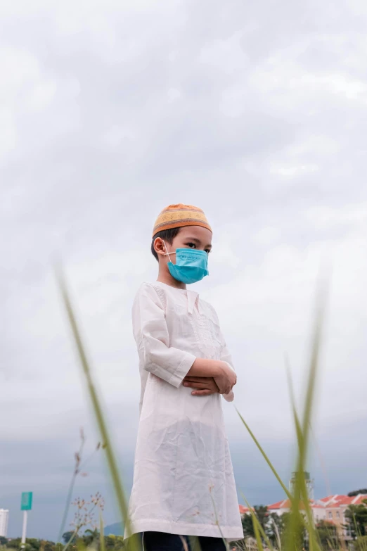 a boy with a surgical mask standing in the grass