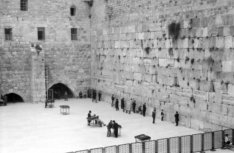 two men stand at a bench in front of the stone wall