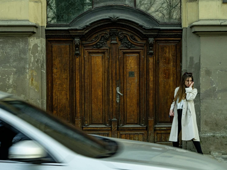 woman wearing coat next to wooden door in urban setting