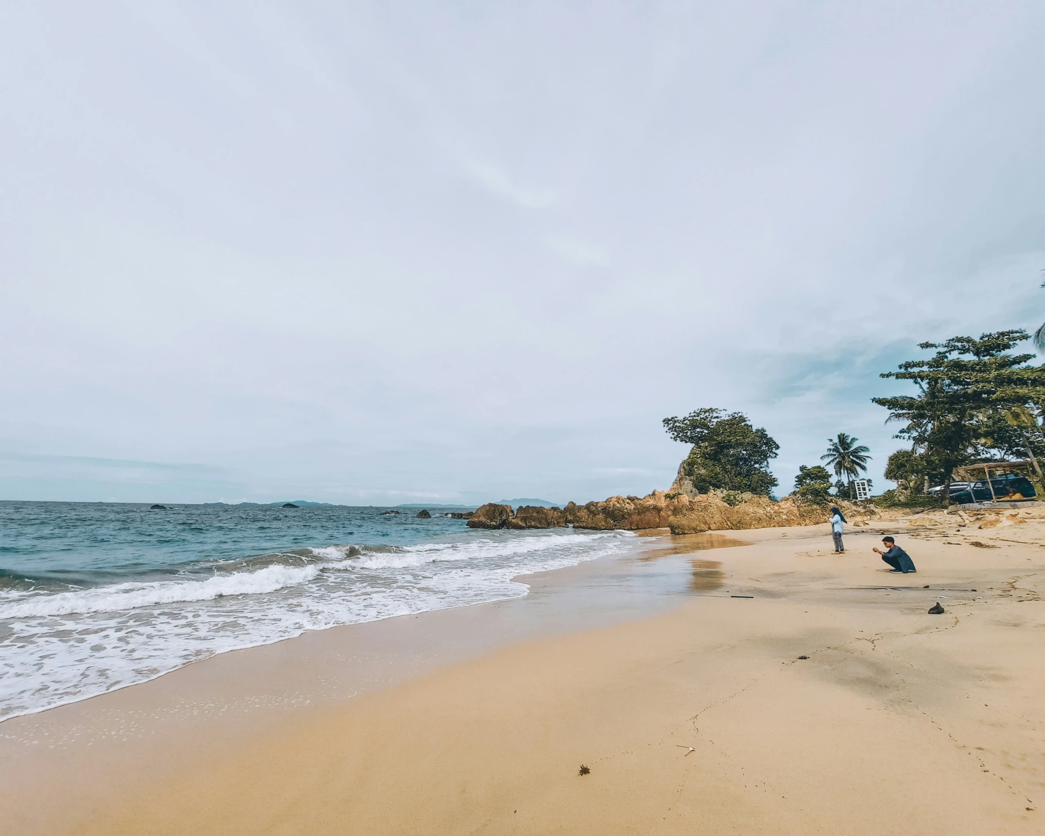 people walking along a sandy beach with the ocean behind them