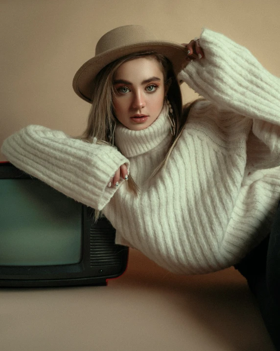 a woman in white sweater and hat with arm on tv