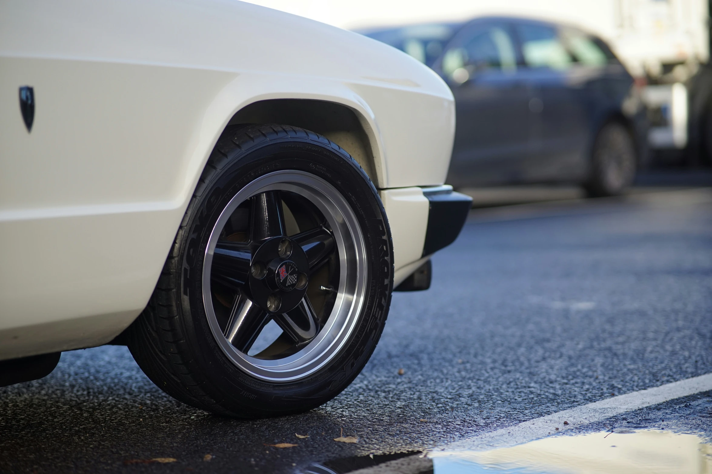 white car with black wheels parked near two cars