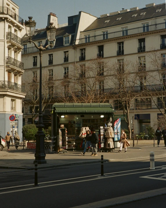 several people walking past an open air market in front of buildings