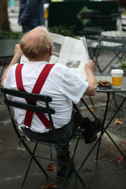 an elderly man is reading a newspaper in the park