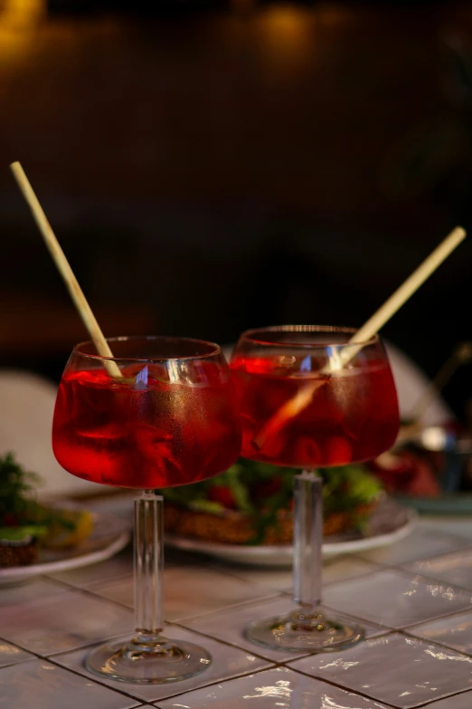 two red drinks and strawberries are sitting on two clear glasses