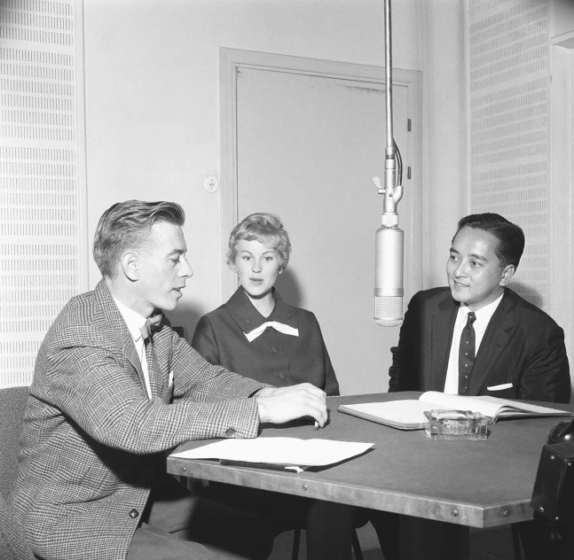 a man holding a note in his right hand while sitting at a table with two women