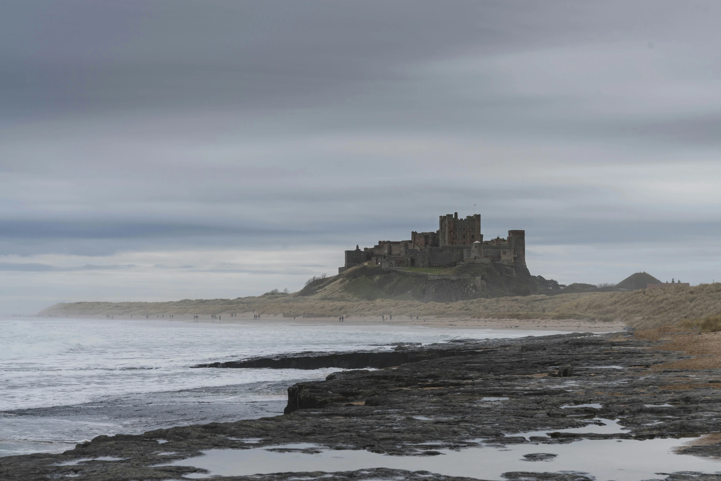 an old castle in the background of water with rocks around it