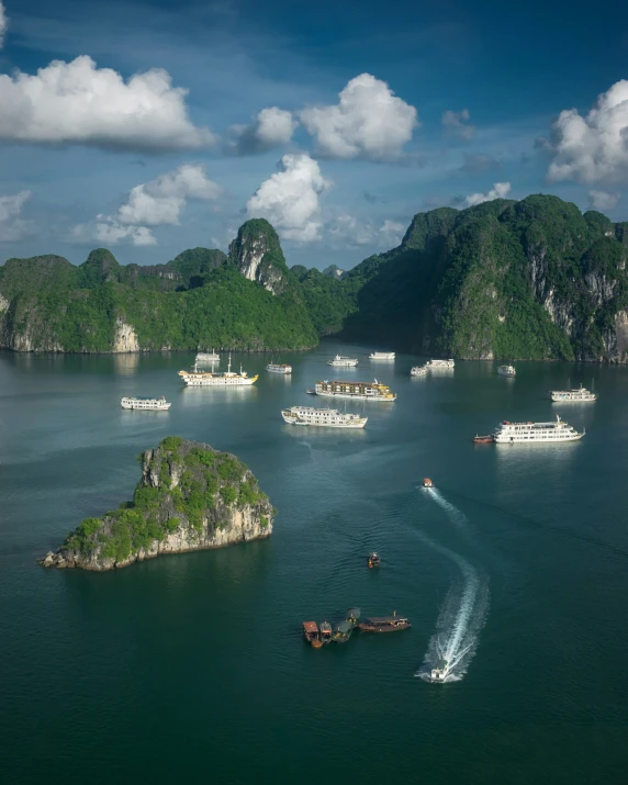 small group of boats traveling across blue water in front of rocky cliffs