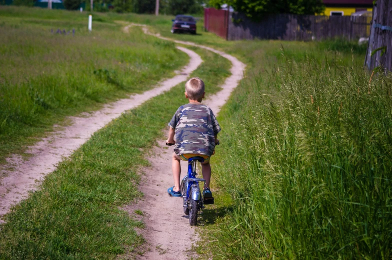 a little boy riding on the back of a bike down a road