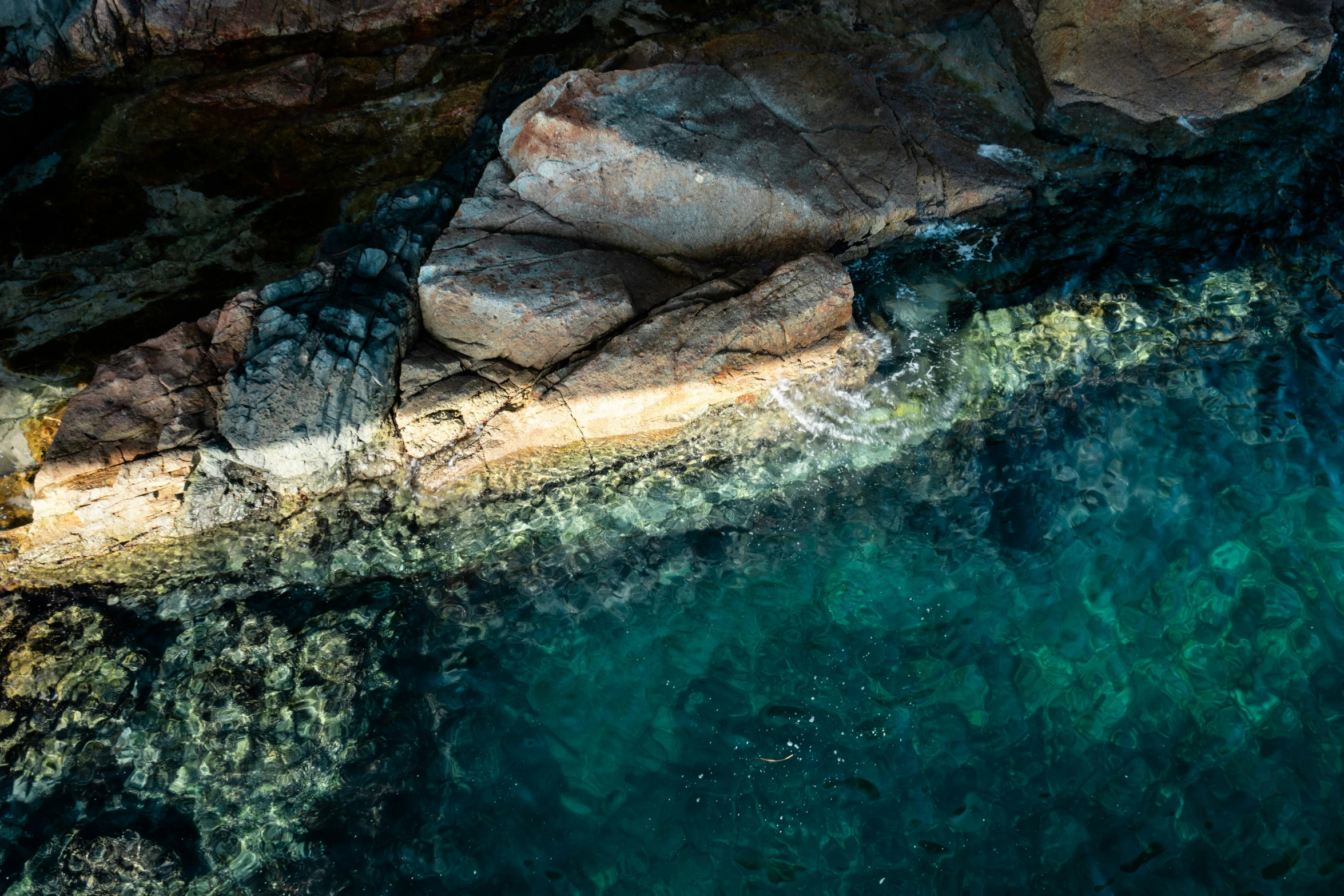 an aerial view of a green ocean with the rocks underneath