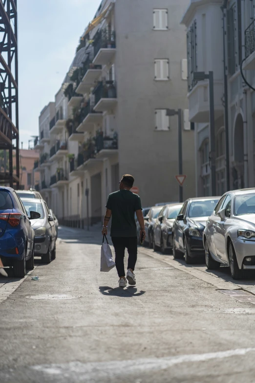 a man is walking down a street with several cars parked in front of him