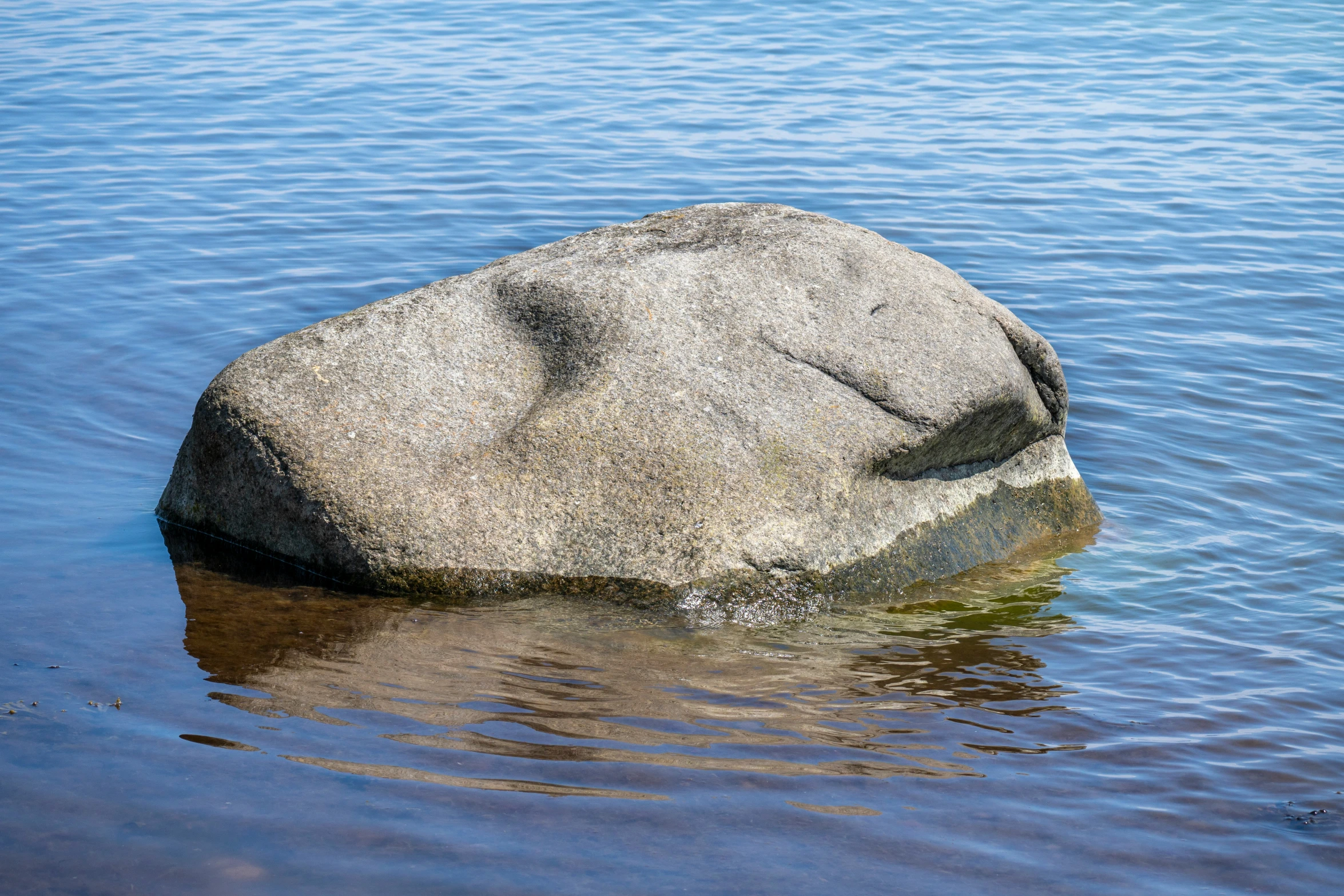 a rock in the water with some sand in the background