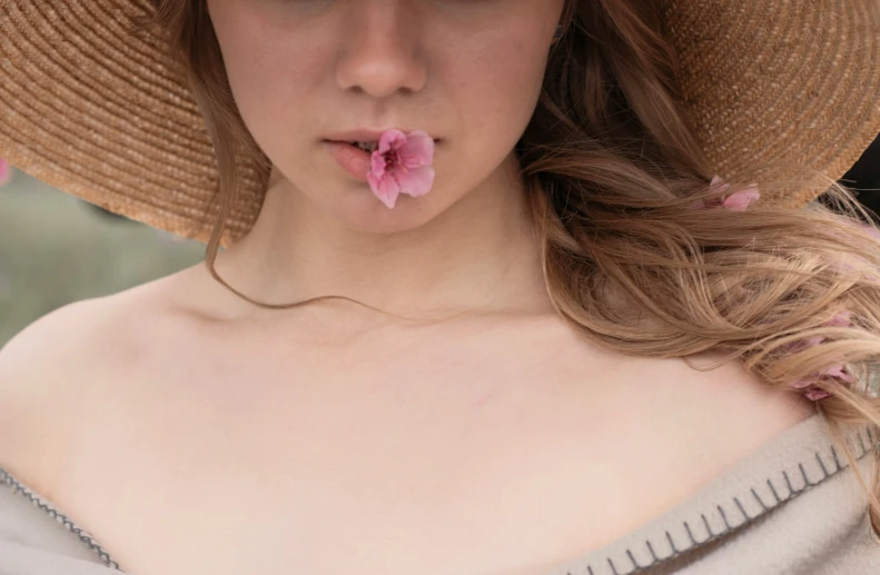 the woman wearing hat has a pink flower in her mouth