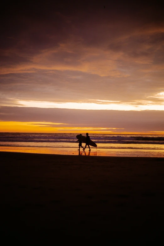 two surfers walk on the beach near the sunset