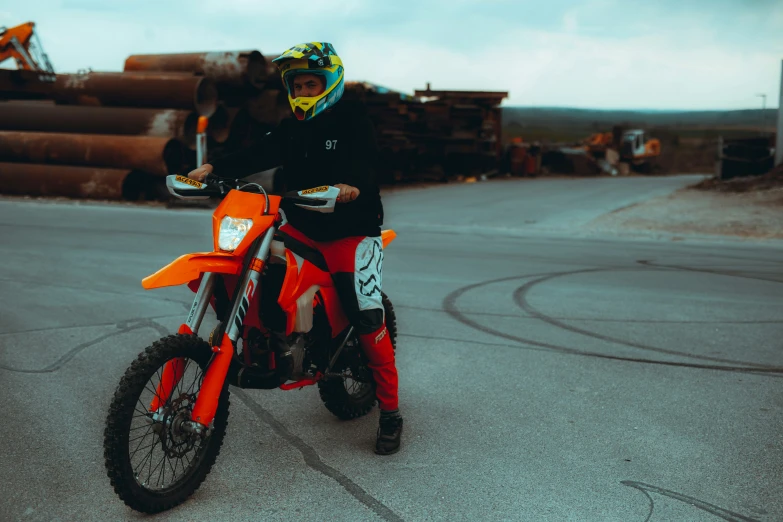 a young man riding a dirt bike next to a pile of logs