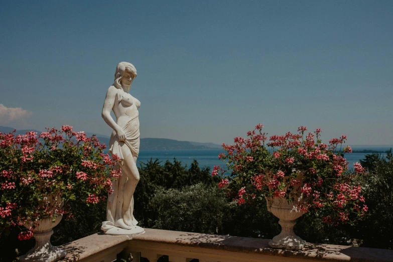 a white statue on a wall in front of flowers and bushes