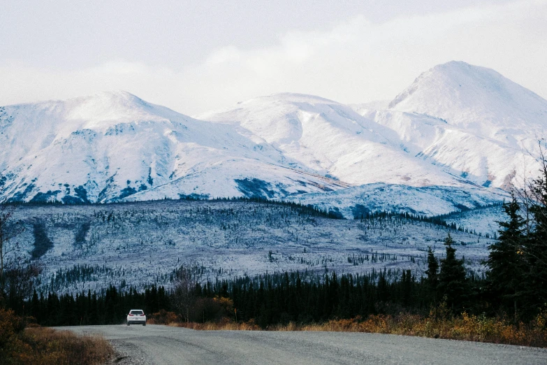 a truck on a country road in front of some snow - capped mountains