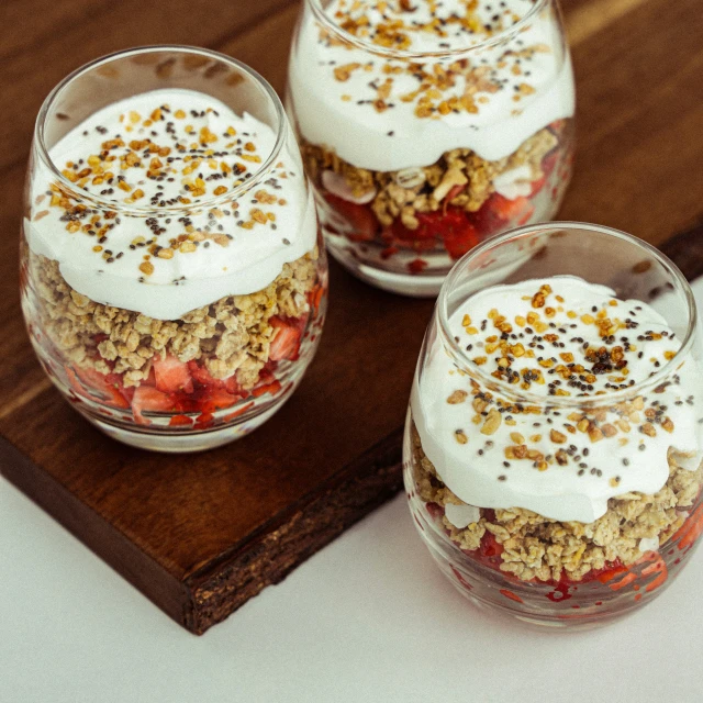 three glasses filled with fruit covered dessert sitting on top of a wooden  board