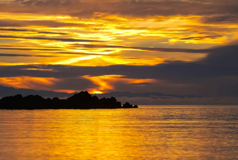 a sunset seen over the ocean with an island in the middle of it