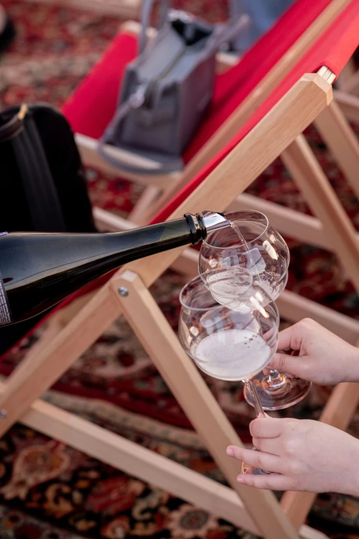 someone holding a bottle of wine in front of a small wine glass on a table