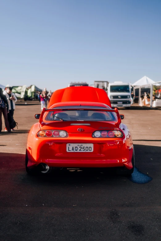 red sports car parked at a festival in the shade