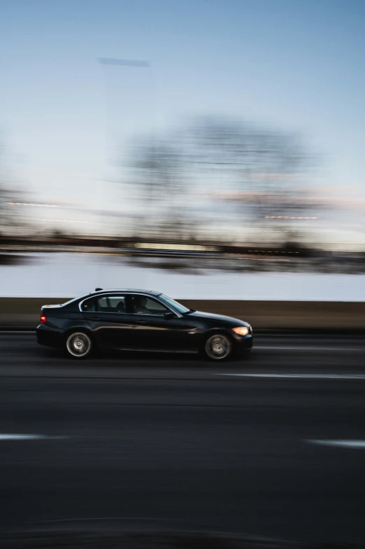 a black car driving on a road with trees and water in the background