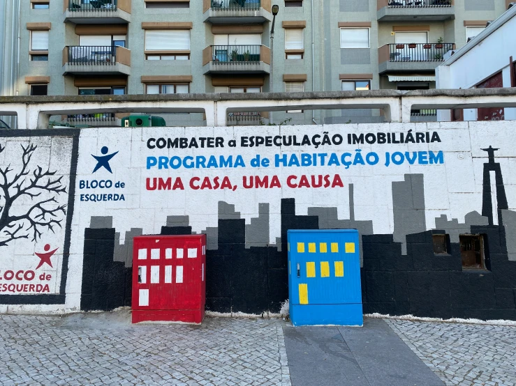 a wall painted with city buildings and doors painted blue, red, yellow, and white