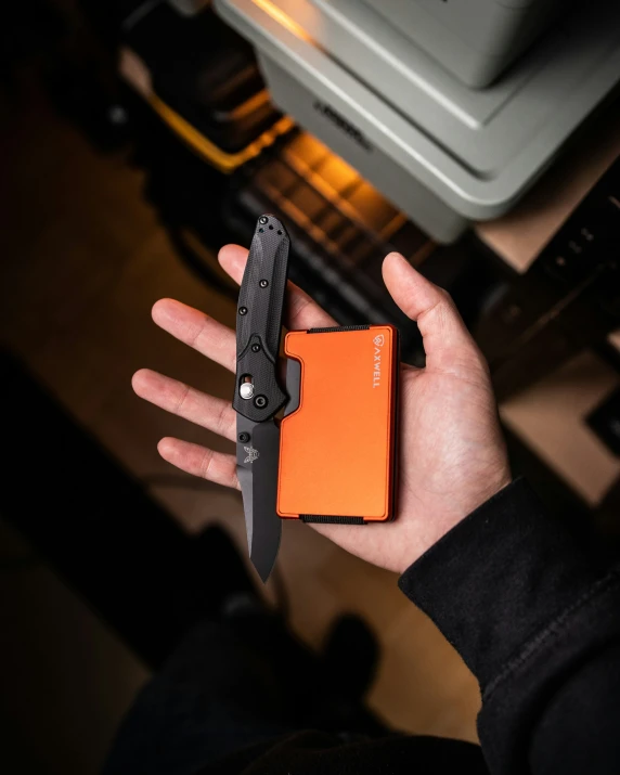 a man holds his orange pocket knife next to the open fire