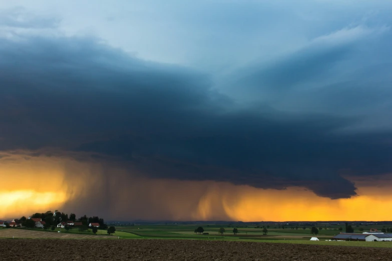 a field with trees in the background and a storm rolling in behind