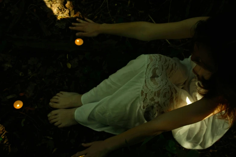 a woman wearing a white dress laying in the grass with candles on the ground