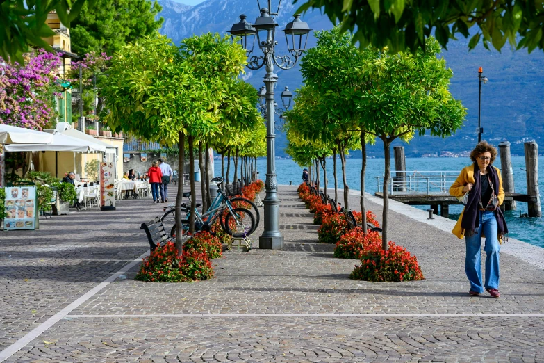 a woman walking on the pathway to a pier with flowers and trees lined in rows of flower pots