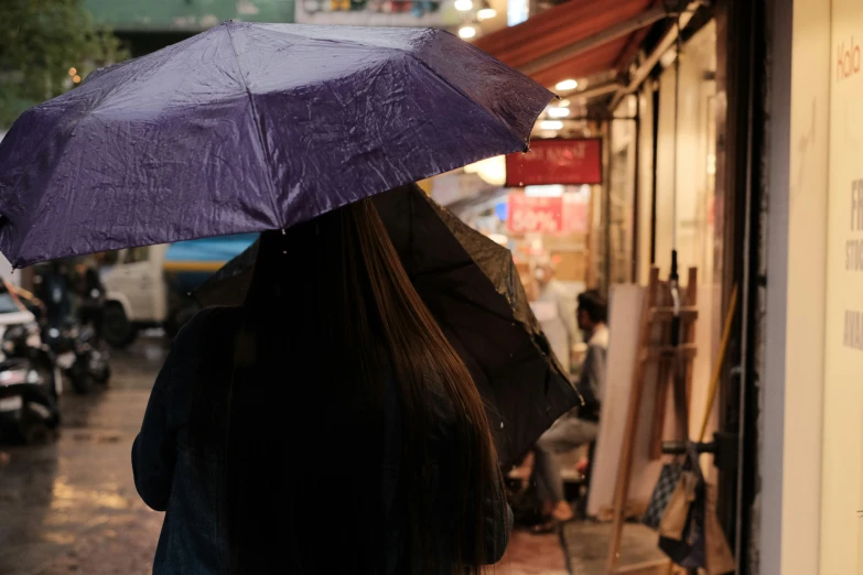 back view of a woman with purple umbrella in front of shopfronts