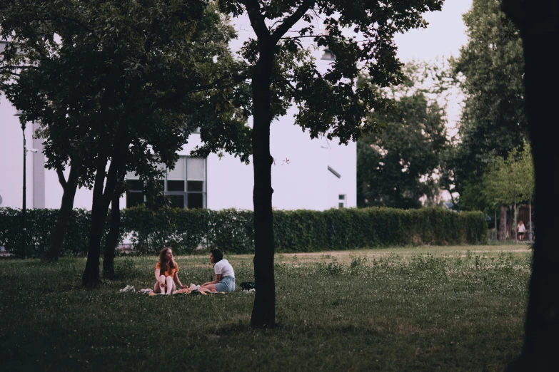 two people sitting on the grass in front of some trees