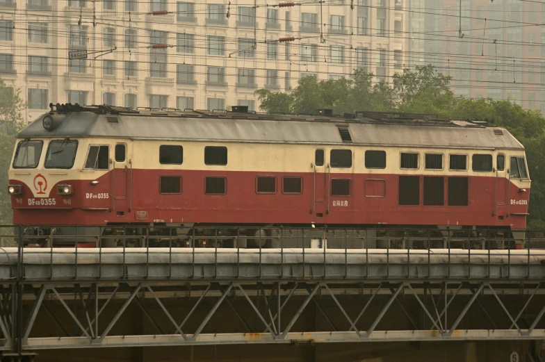 a passenger train crossing over a bridge and next to a tall building