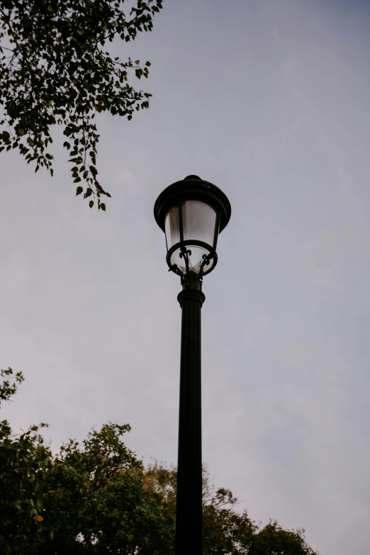 a black lamppost near some trees against a cloudy sky