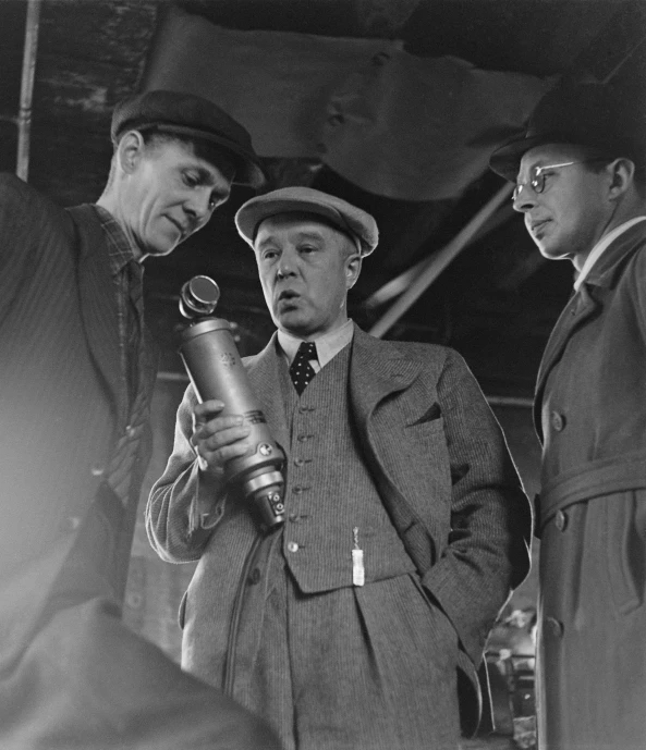 three men standing in a room one is holding a bottle