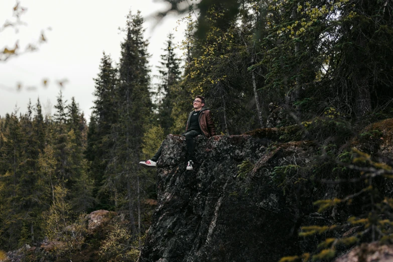 a man sitting on top of a rock next to trees