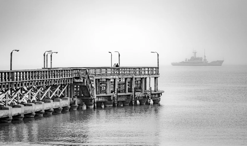 a wooden pier with lights on and a large ship in the background