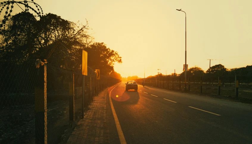 a view of the sun in front of a car on a road