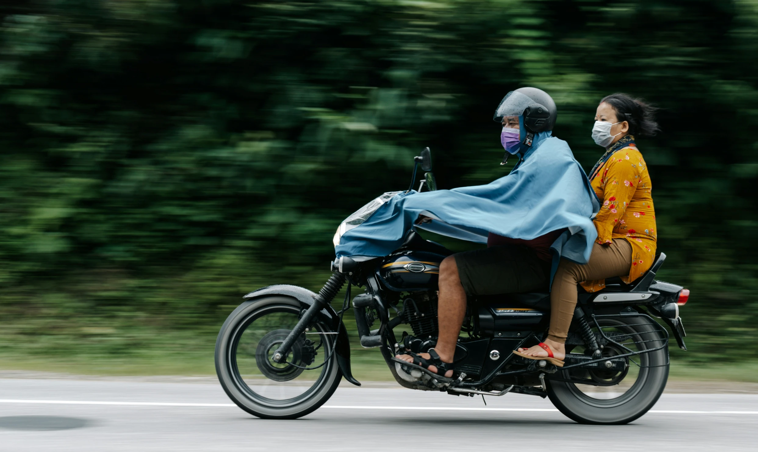 two people on a motorcycle with trees in the background