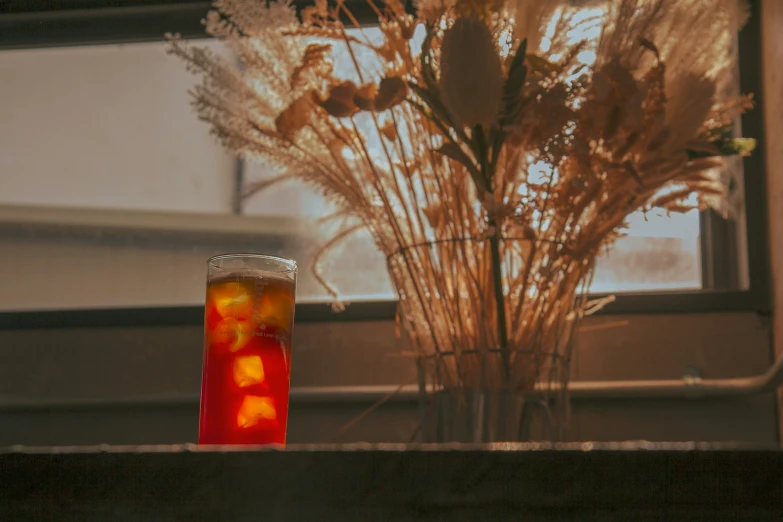 an image of some flowers and drink near the window