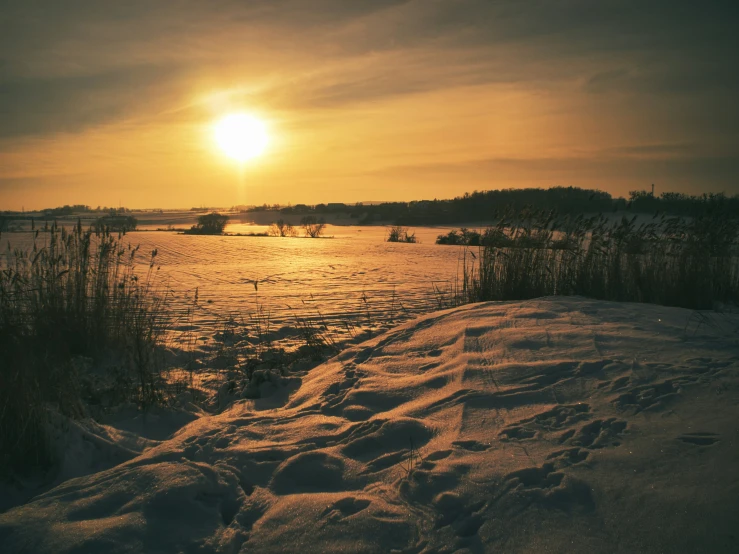 a sunset over a small body of water with snow on the ground
