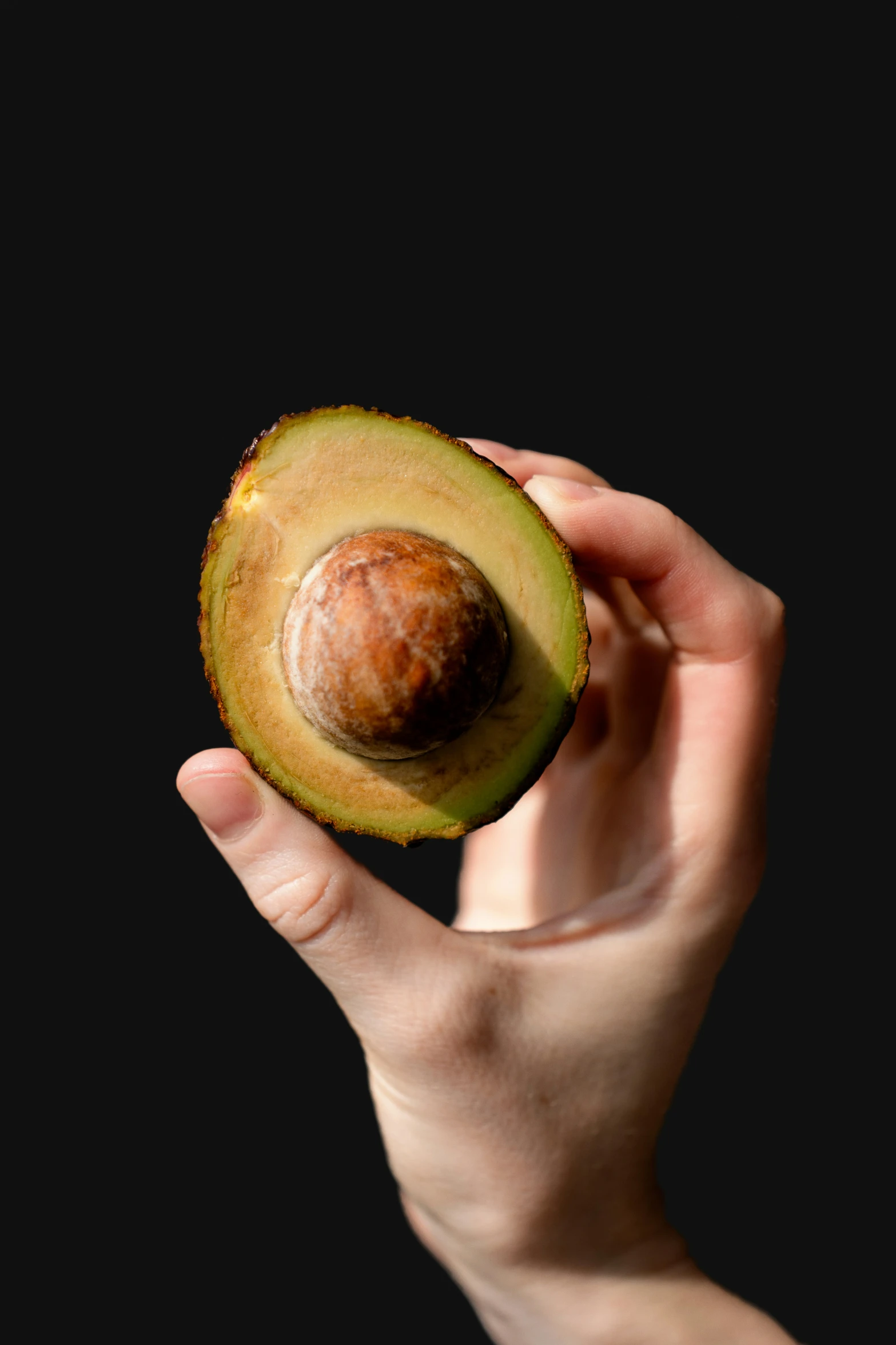 a hand holds up an avocado in the dark